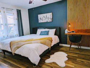 A bedroom with a bed, a desk, a chair, and a cityscape painting on the wall. - Colony Home for Family Groups - Patio, Workspace (Marietta)