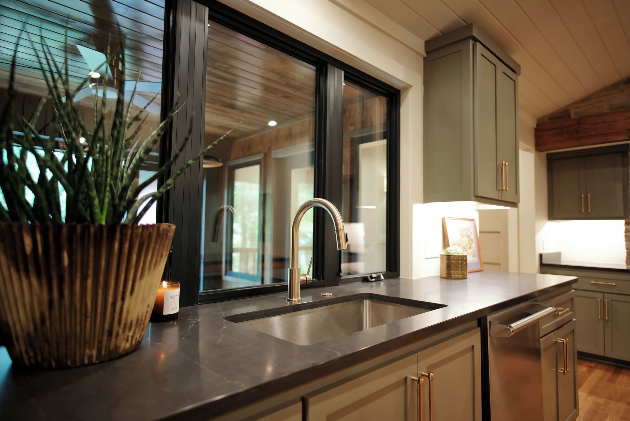 A modern kitchen with a large window, stainless steel sink, and wooden cabinets.