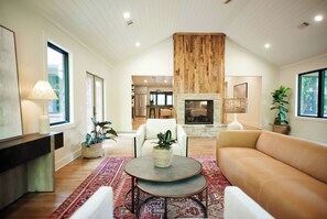 A spacious living room with a fireplace, a dining area, and a kitchen in the background. - Charming 4-bedroom MidCentury Bungalow—Brand New! (Oxford)