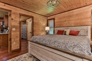 A wooden room with a bed, a nightstand, a lamp, and a door leading to another room. - Chestnut Hills Lodge by Mountain Oasis | Luxury Blue Ridge Cabin (Blue Ridge)