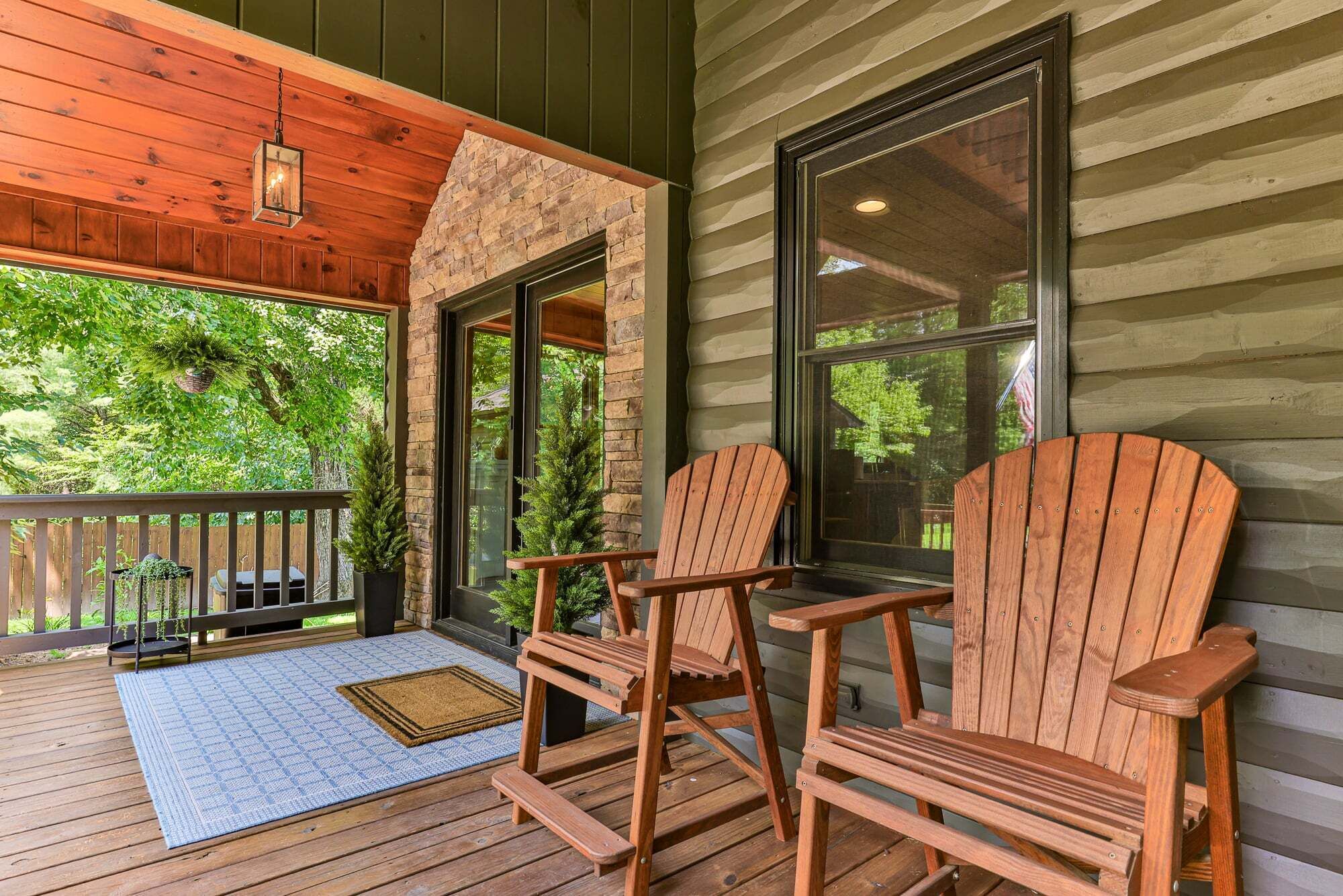 A wooden deck with Adirondack chairs, a stone wall, and a large window.