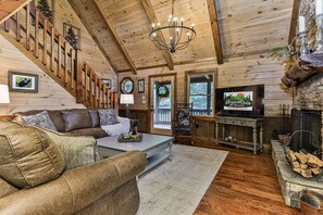 A cozy cabin interior with a fireplace, a television, and a staircase leading to an upper level. - Chestnut Hills Lodge by Mountain Oasis | Luxury Blue Ridge Cabin (Blue Ridge)