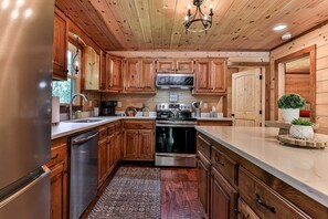 A kitchen with wooden cabinets, stainless steel appliances, and a marble countertop. - Chestnut Hills Lodge by Mountain Oasis | Luxury Blue Ridge Cabin (Blue Ridge)