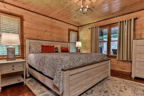 A wooden-paneled bedroom with a bed, nightstands, a lamp, and a view of the outdoors. - Chestnut Hills Lodge by Mountain Oasis | Luxury Blue Ridge Cabin (Blue Ridge)