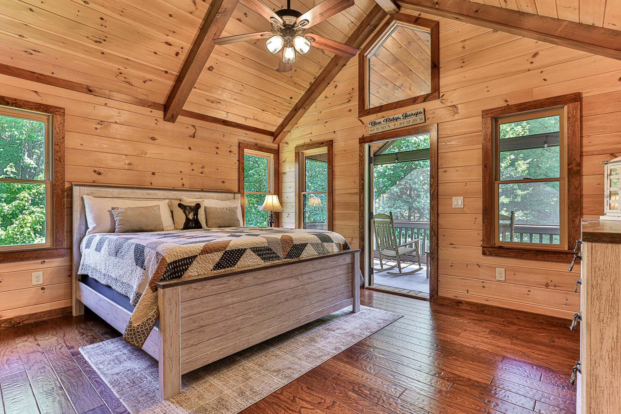 Ein Schlafzimmer einer Holzhütte mit einem Bett, einem Nachttisch, einer Lampe und einem großen Fenster.