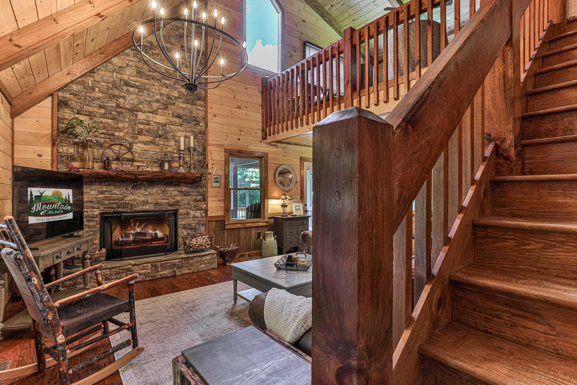 L’intérieur d’une cabane avec une cheminée en pierre, un escalier en bois et un téléviseur fixé au mur.