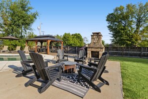 Un patio exterior con chimenea de piedra, sillones y una piscina.