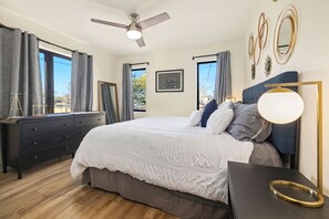 Un dormitorio con cama, cómoda, mesita de noche, ventilador de techo y ventana con cortinas.