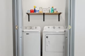 A laundry room with two washing machines and a shelf with cleaning supplies. - Private pool, walk to downtown Springdale, dogs welcome, close to U of A. (Springdale)