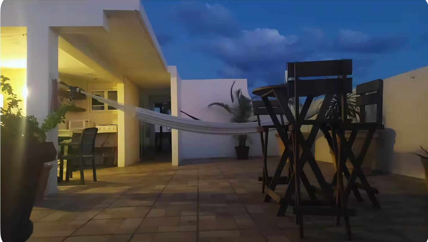 Uma área de pátio com uma rede, móveis de exterior e vista para o interior de um edifício.