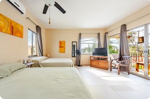 Una camera d'albergo con due letti, una televisione, un ventilatore e un balcone con una sedia.