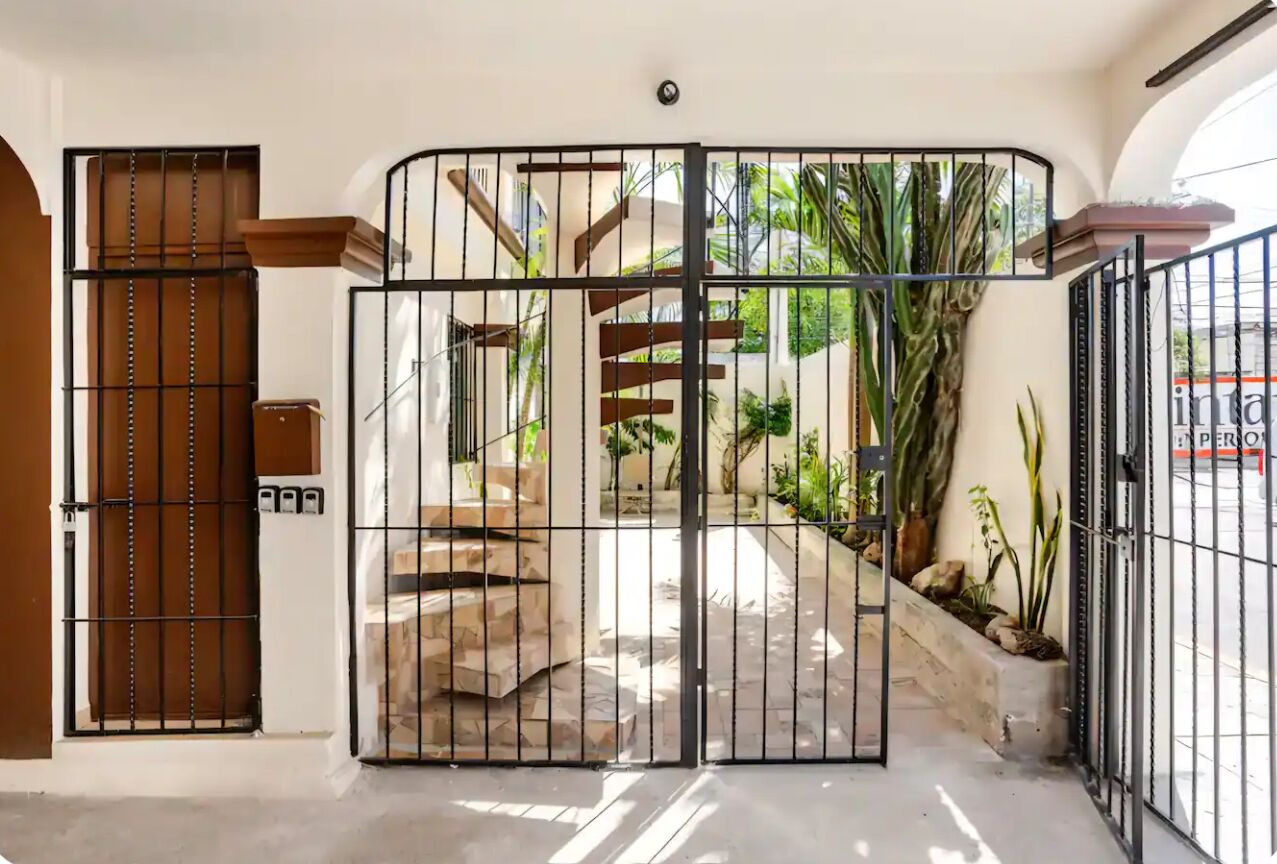Une entrée fermée par un portail, avec un escalier menant à un espace abrité agrémenté de plantes.