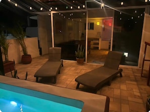 An outdoor patio with two lounge chairs, a pool, and a glass door leading to an interior space. - La Sirenita: 2-bed studio with rooftop lounge access minutes from 5 Avenida (Playa del Carmen)