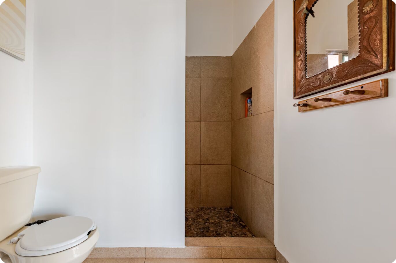 A bathroom with a toilet, shower, and a mirror with a decorative frame.