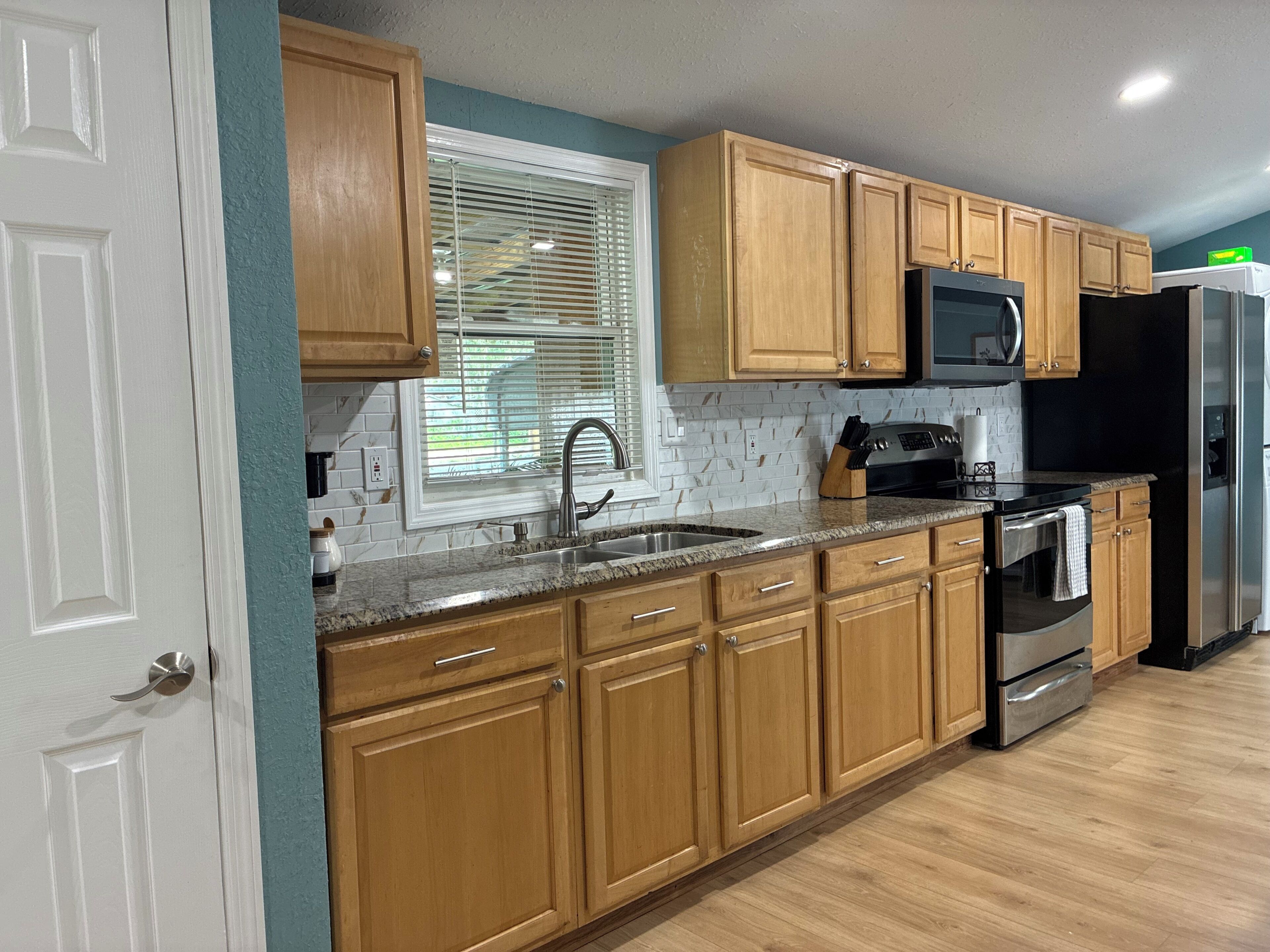 A kitchen with wooden cabinets, a stainless steel sink, a microwave, and a refrigerator.