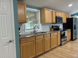 A kitchen with wooden cabinets, a stainless steel sink, a microwave, and a refrigerator.