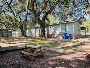 A mobile home with a porch, a picnic table, and a trash bin.