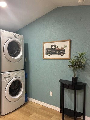 A laundry area with stacked washers and dryers, a framed picture of a truck, and a potted plant on a small table.