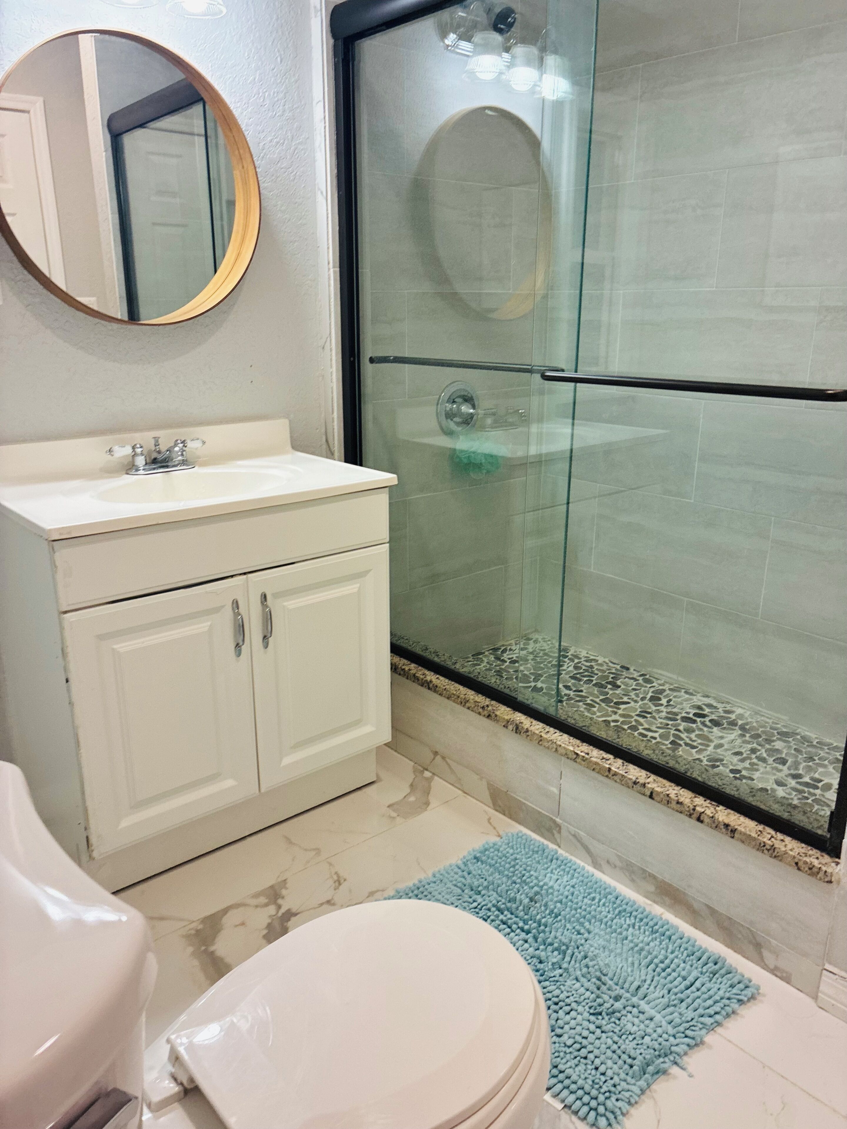 A bathroom with a white sink, a mirror, a toilet, and a glass-enclosed shower area.
