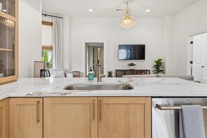 A modern kitchen with a marble countertop, wooden cabinets, a stainless steel sink, and a built-in dishwasher.