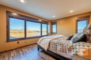 A bedroom with a large bed, multiple windows, and a view of a desert landscape.