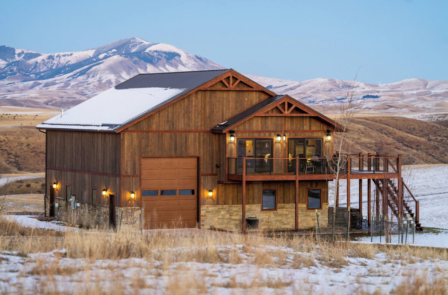 A rustic cabin with a large garage, a balcony with outdoor seating, and a scenic mountain backdrop.