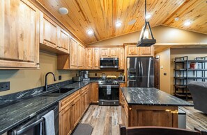 A kitchen with wooden cabinets, a black countertop, stainless steel appliances, and a hanging light fixture.
