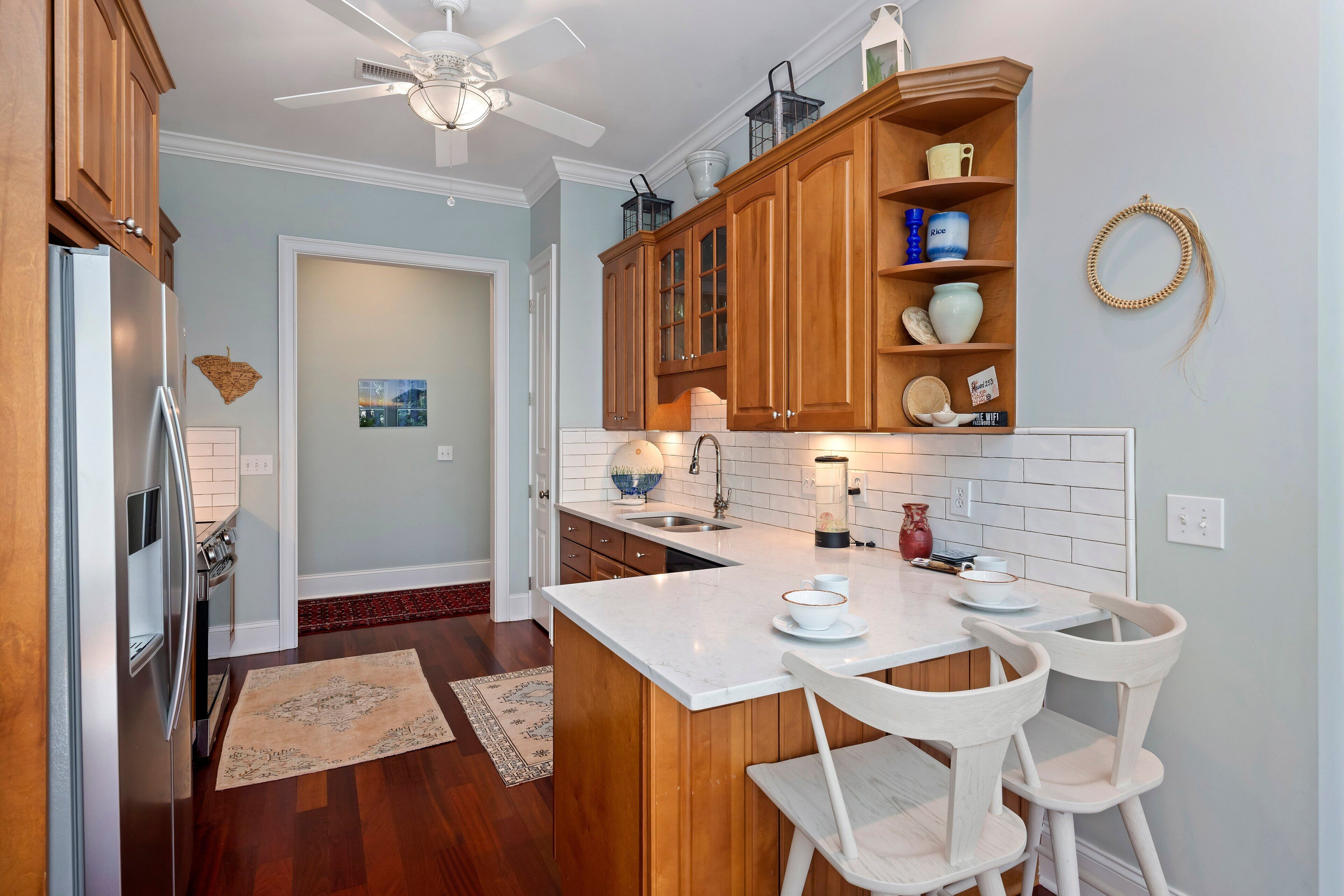 A modern kitchen with wooden cabinets, a white countertop, and a dining area with two white chairs.