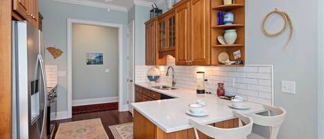 A modern kitchen with wooden cabinets, a white countertop, and a dining area with two white chairs.