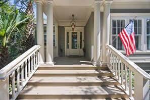 Eine Veranda mit einer Treppe, die zu einer Tür führt, flankiert von weißen Säulen und Geländern, mit einer amerikanischen Flagge.