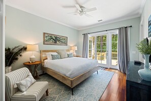 Een slaapkamer met een bed, nachtkastjes, een stoel, een plafondventilator en een groot raam met gordijnen.