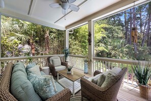 Ein überdachter Außenbereich mit Korbmöbeln, einem Deckenventilator und Blick auf einen dichten Wald.