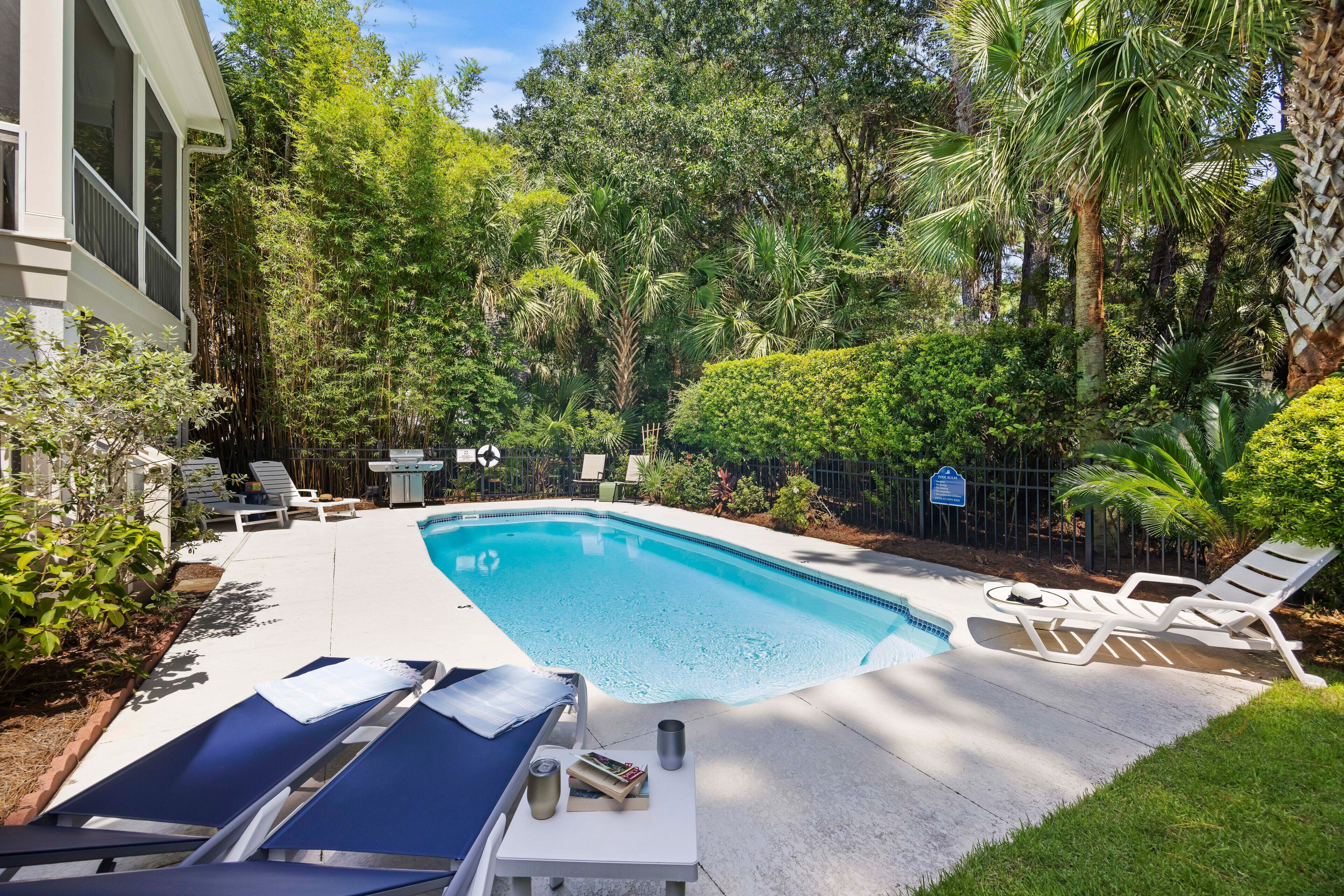 A swimming pool with lounge chairs and a grill area surrounded by lush greenery.