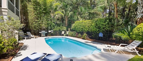 A swimming pool with lounge chairs and a grill area surrounded by lush greenery.
