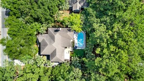 Luchtbeeld van een huis met zwembad, omringd door dichte bomen.