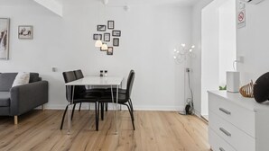 Uma sala de estar moderna com área de jantar, um sofá cinza, uma mesa de jantar branca com cadeiras pretas e um armário branco com gavetas.
