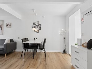 Ein modernes Wohnzimmer mit Essbereich, einem grauen Sofa, einem weißen Esstisch mit schwarzen Stühlen und einer weißen Kommode mit Schubladen.