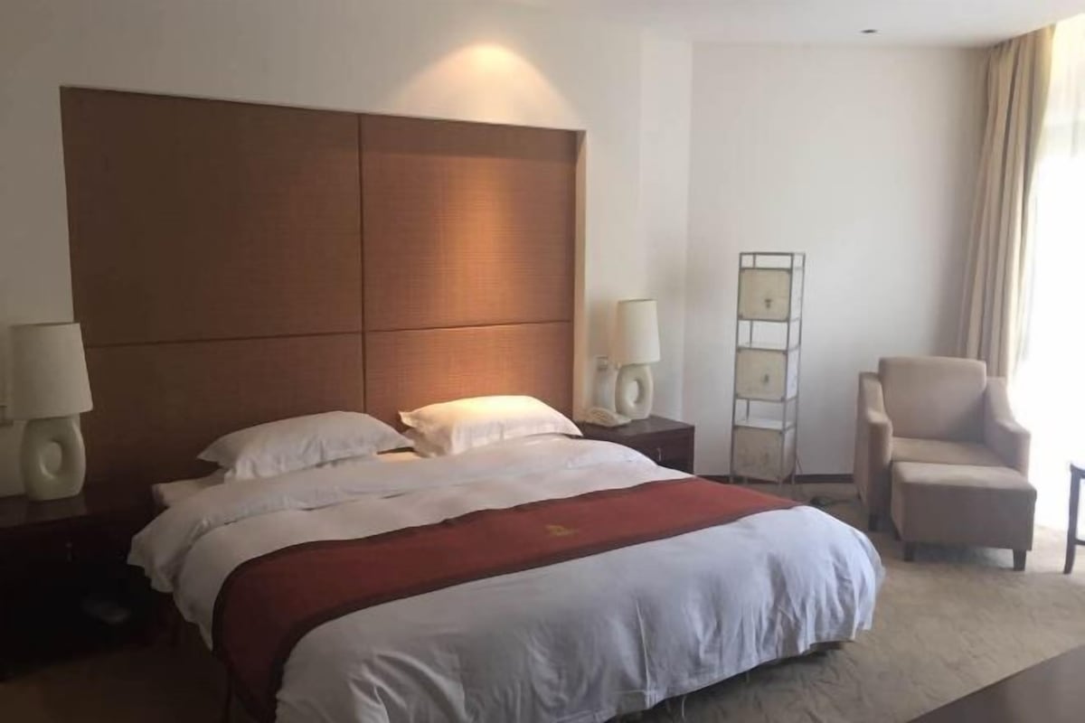 A hotel room with a large bed, two bedside tables with lamps, a chair, and a floor lamp.