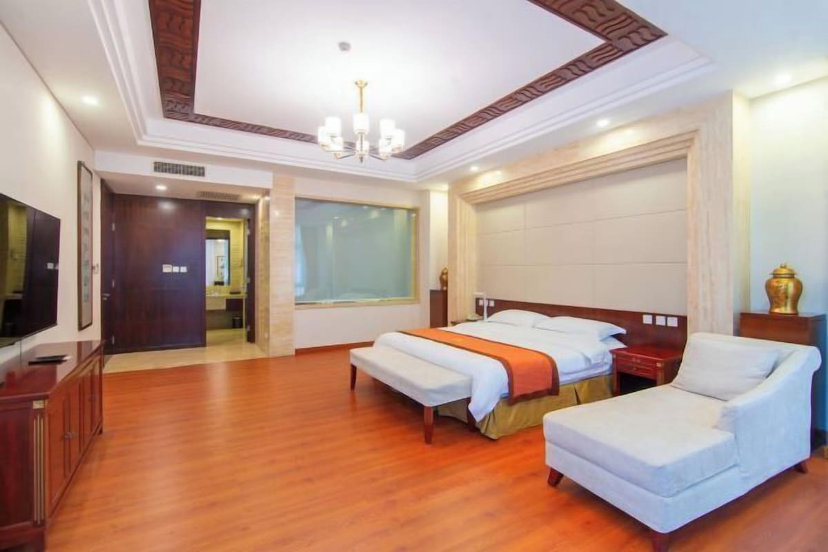 A hotel room with a large bed, a sofa, a television, and a chandelier.