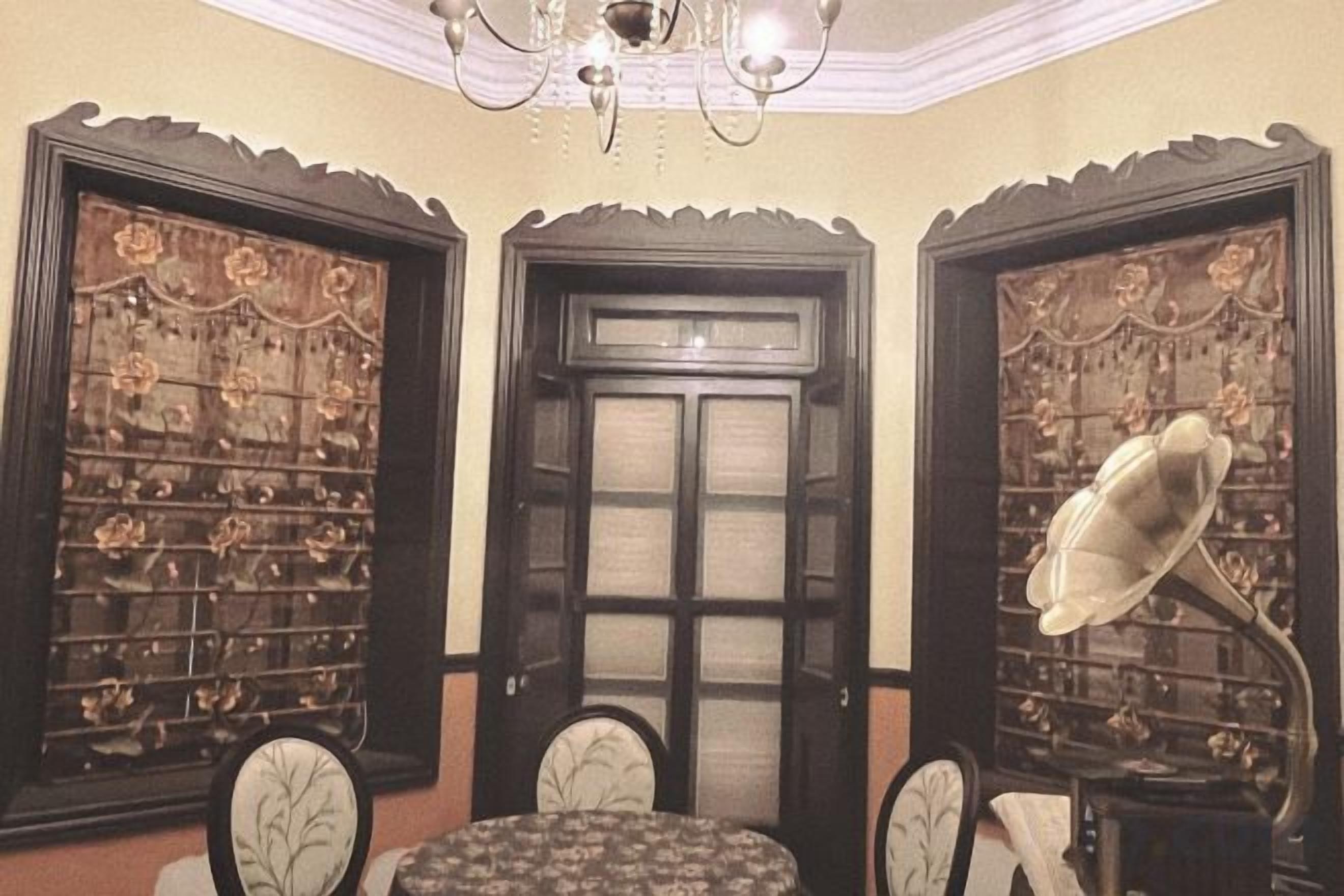 A room with a round table, two chairs, a chandelier, and ornate doors with intricate designs.