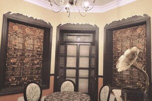 A room with a round table, two chairs, a chandelier, and ornate doors with intricate designs.