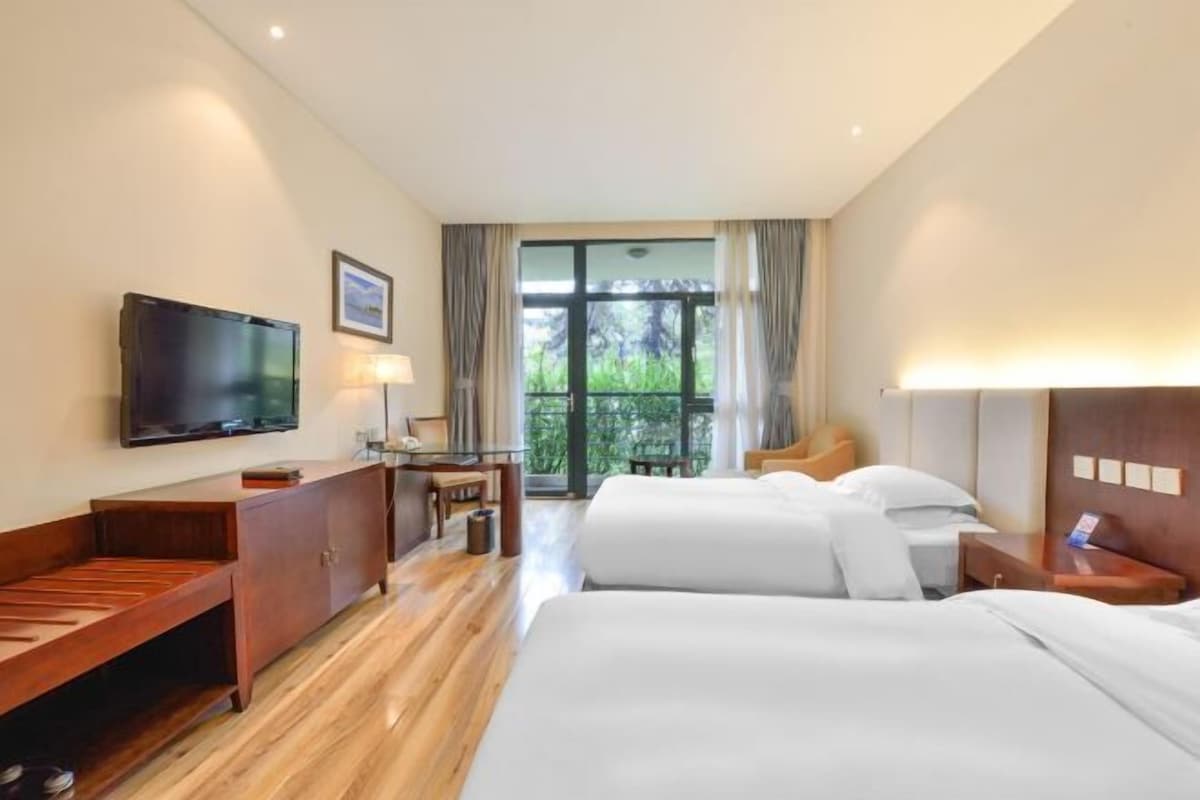 A hotel room with a bed, a desk, a television, and a window with a view of greenery.