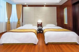 Habitación de hotel con dos camas, piso de madera, una mesita de noche con lámpara y un ventanal con cortinas.