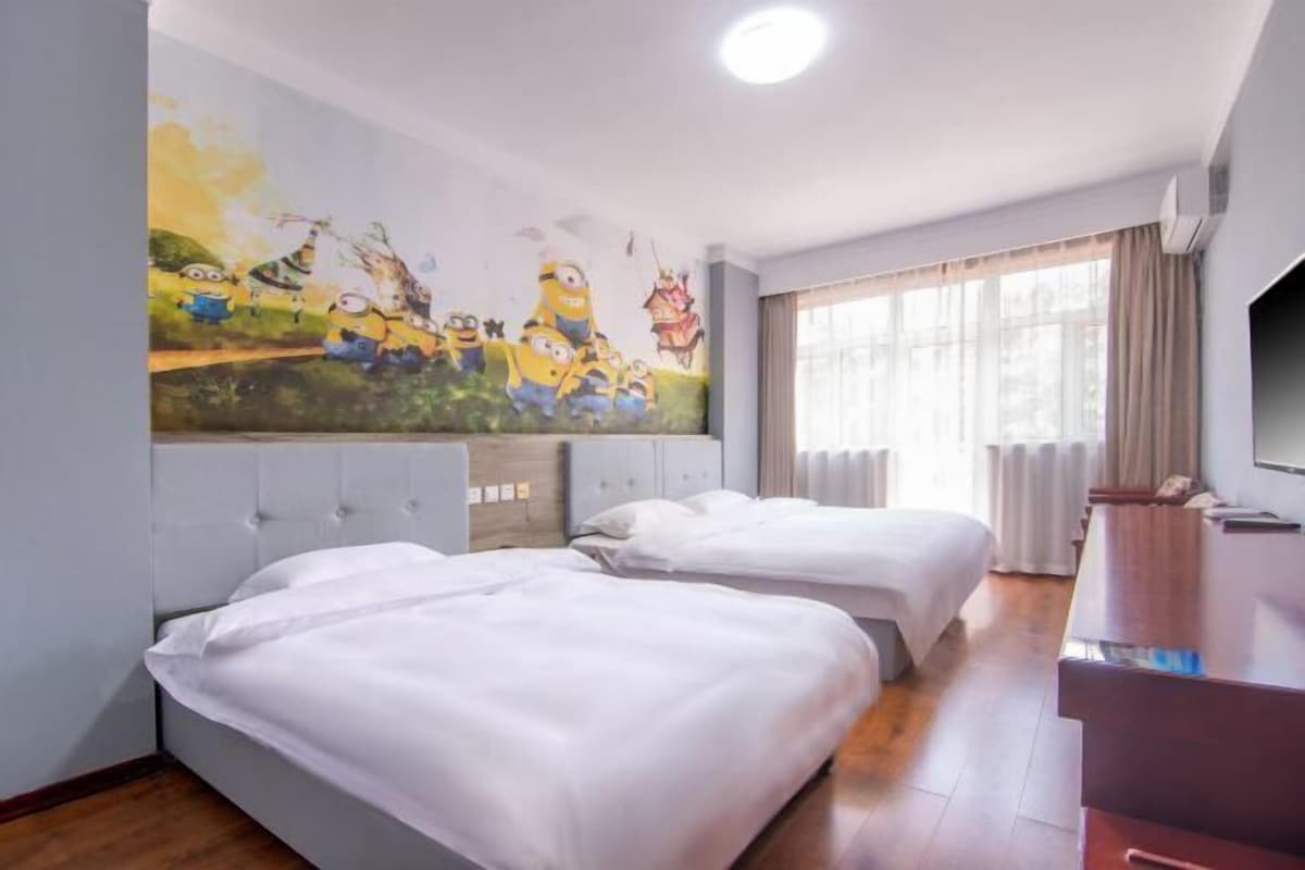 A hotel room with two beds, a large wall mural, a television, and a window with curtains.