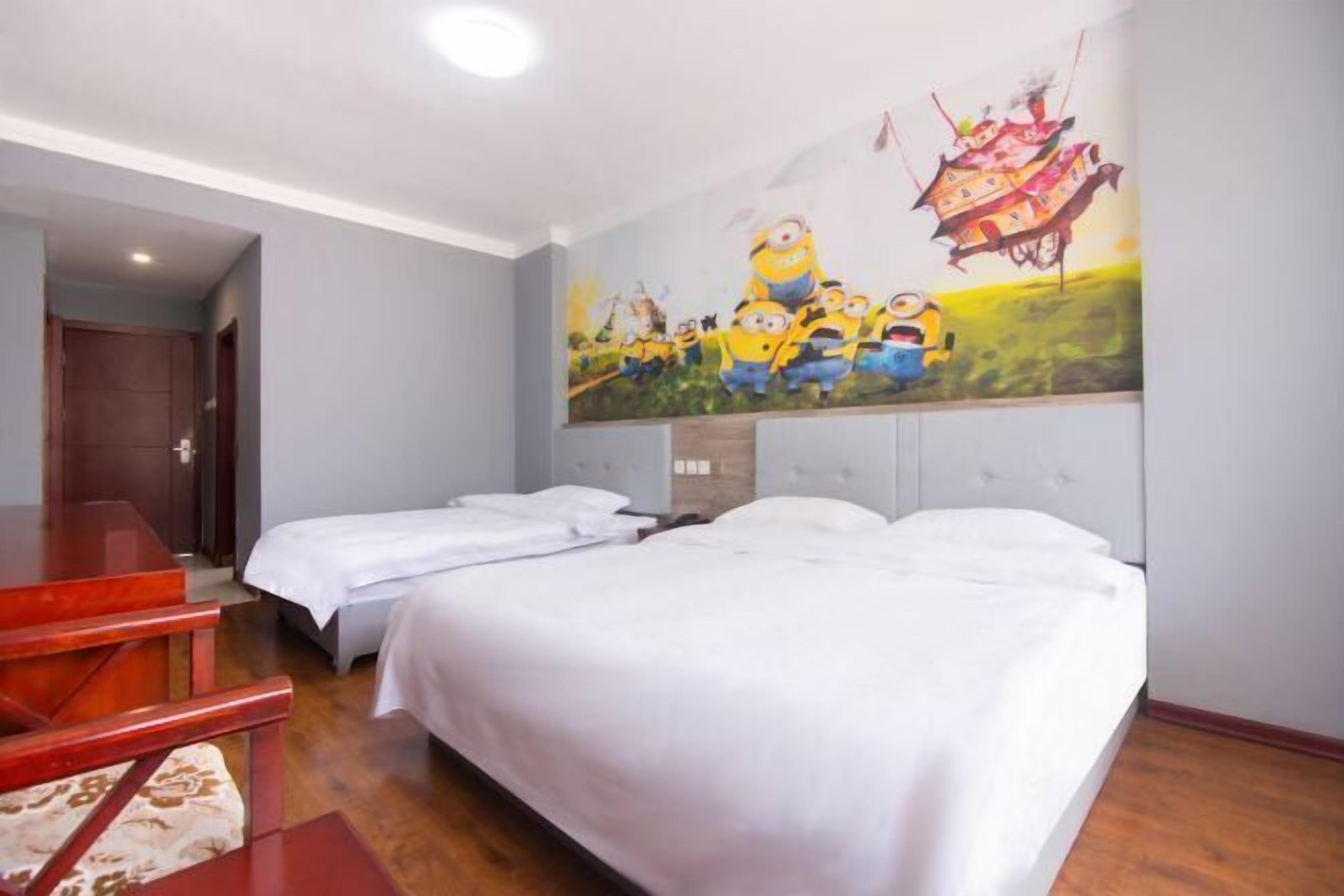 Habitación de hotel con dos camas, un escritorio rojo y un mural de Los Minions en la pared.