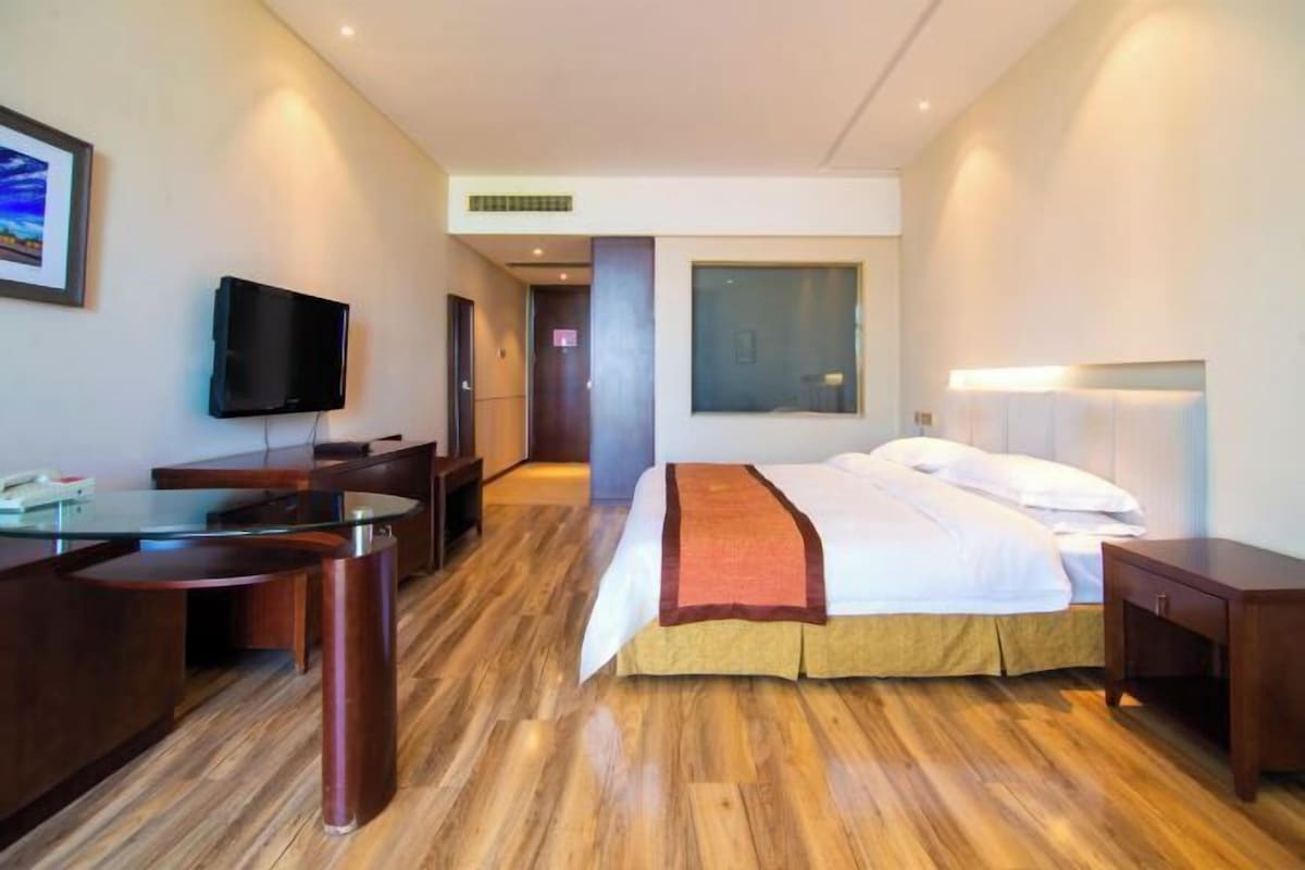 A hotel room with a bed, desk, television, and a view of the city.