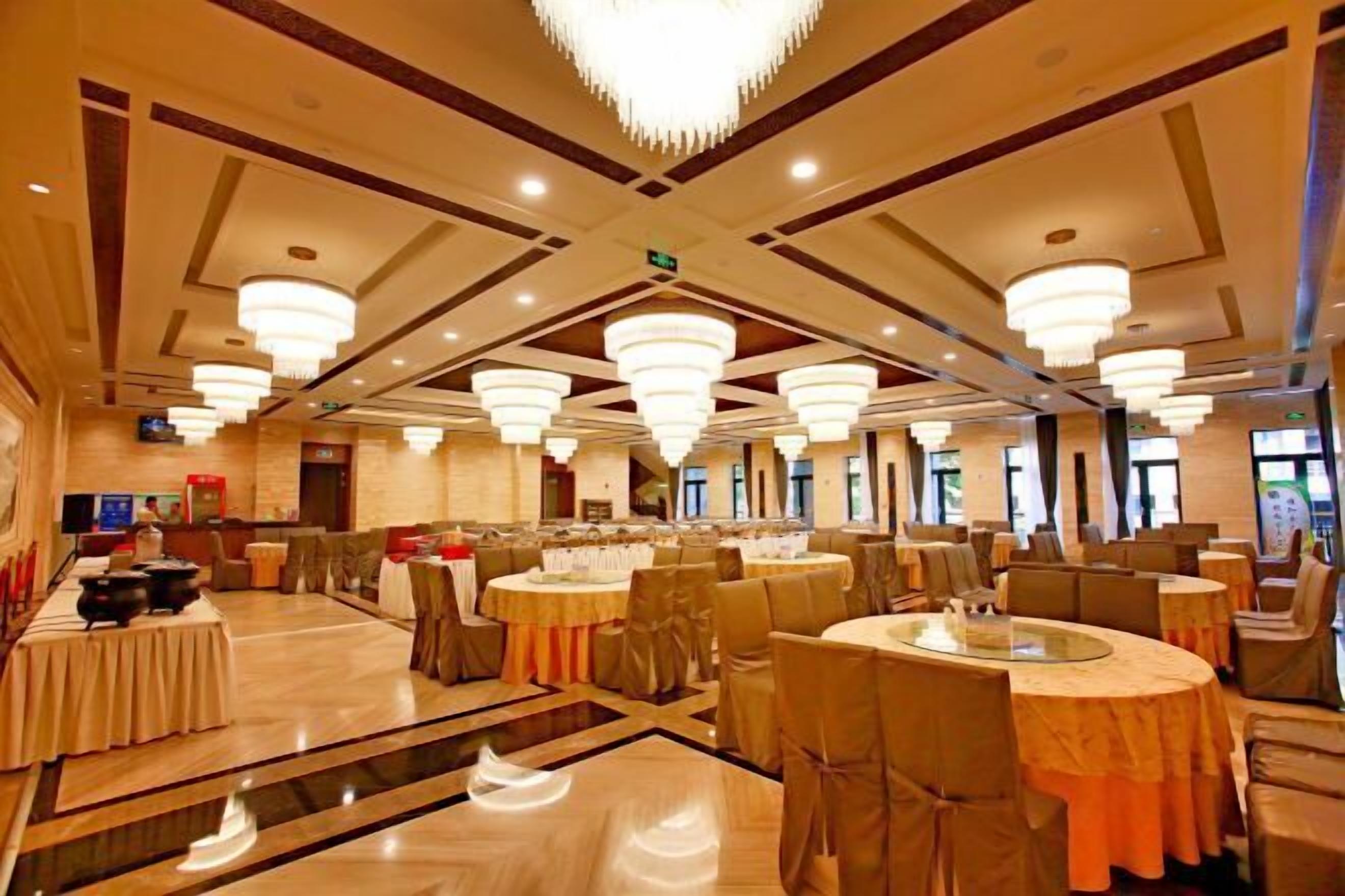 A banquet hall with round tables, chairs, and chandeliers.