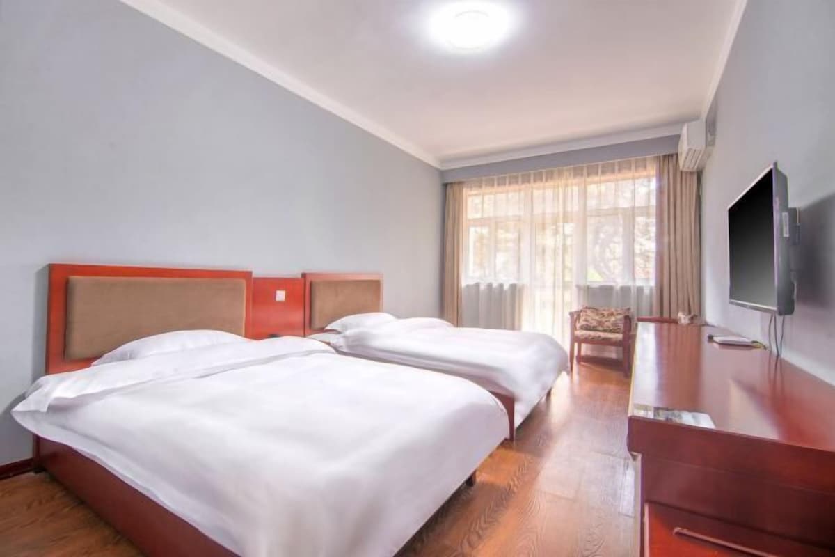 A hotel room with two beds, a TV, and a window with curtains.