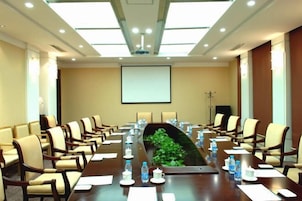 Un salón de conferencias con una larga mesa, sillas, botellas de agua y una pantalla de proyector.