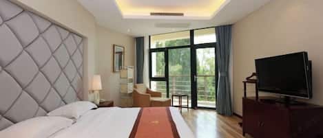 A hotel room with a large bed, a flat-screen TV, a seating area, and a view through the window.